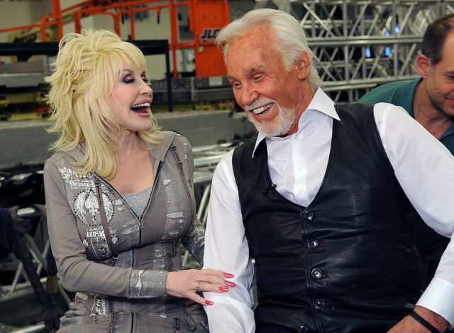 Dolly Parton and Kenny Rogers sit beside each other laughing.