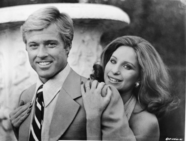 Robert Redford in a suit with Barbra Streisand hugging him from behind.