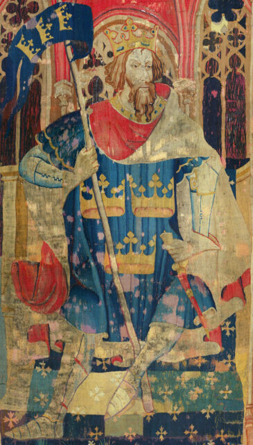 Well worn tapestry of King Arthur on a throne holding a flag.