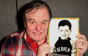 Jerry Mathers in a red plaid shirt holding a picture of himself as a child.