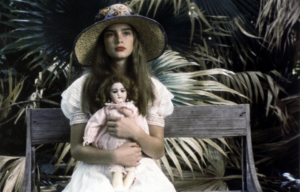 Young Brooke Shields in a dress and hat holding a doll.