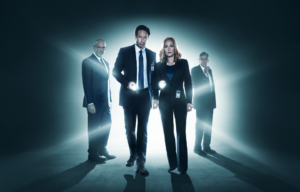 David Duchovny, Gillian Anderson, Mitch Pileggi, and William Davis in black suits backlit by a light.