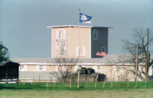 Building with a tank in front of it, a Branch Davidian flag flying, and a sign that reads "Rodney King We Understand."