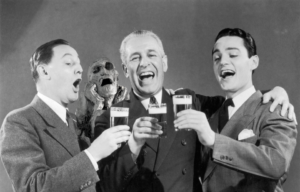 Three men cheering and raising a glass, a mummy behind them at their shoulders.