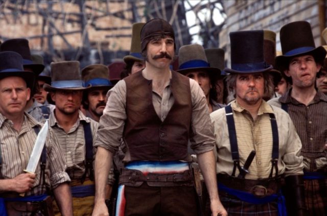 Daniel Day-Lewis as Bill the Butcher surrounded by men in top hats and collared shirts.