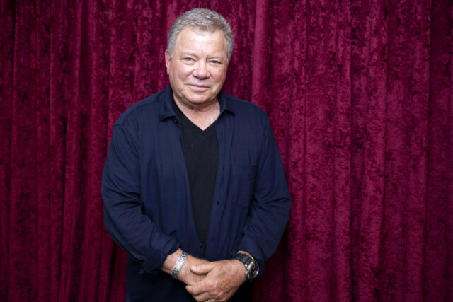 Shatner stands in front of a red velvet curtain