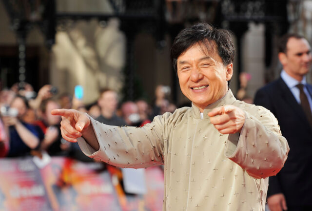 Jackie Chan pointing with both index fingers and smiling.
