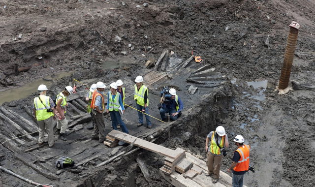 Workers standing around the remains of a wooden sloop