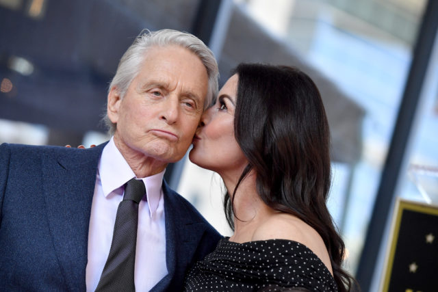 Catherine Zeta-Jones giving Michael Douglas a kiss on the cheek as he purses his lips.