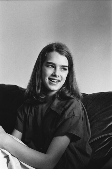 Young Brooke Shields sitting on a couch smiling.