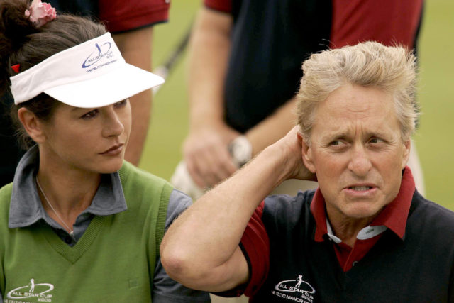 Catherine Zeta-Jones in a visor looking at Michael Douglas scratching his head.