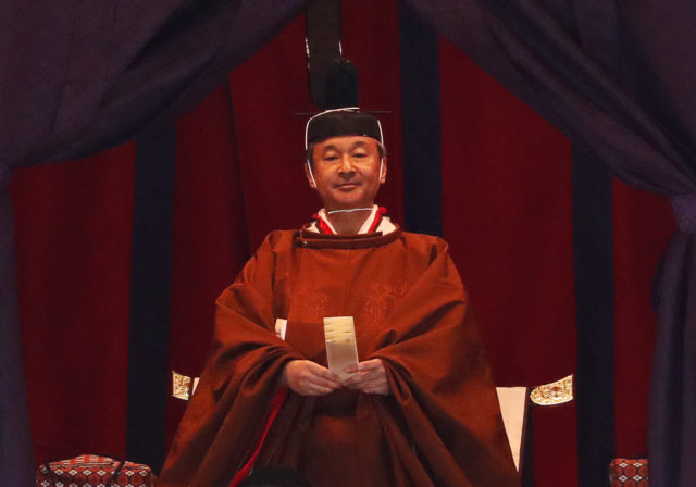 Emperor Naruhito sitting on the chrysanthemum throne in a red gown and headpiece.