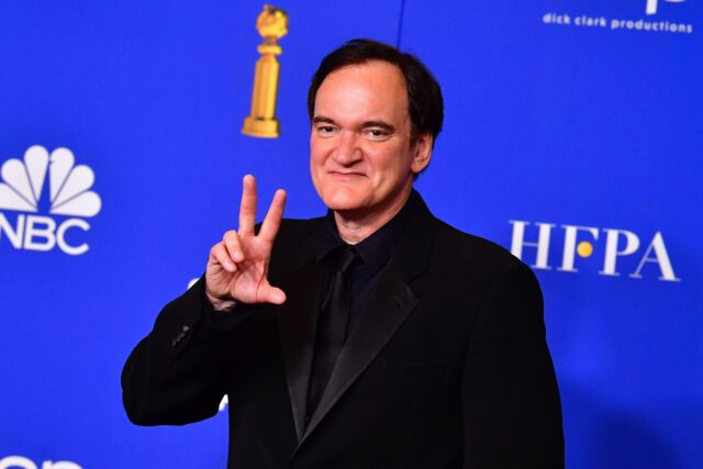 Headshot of Quentin Tarantino holding up two fingers and his thumb in salute.