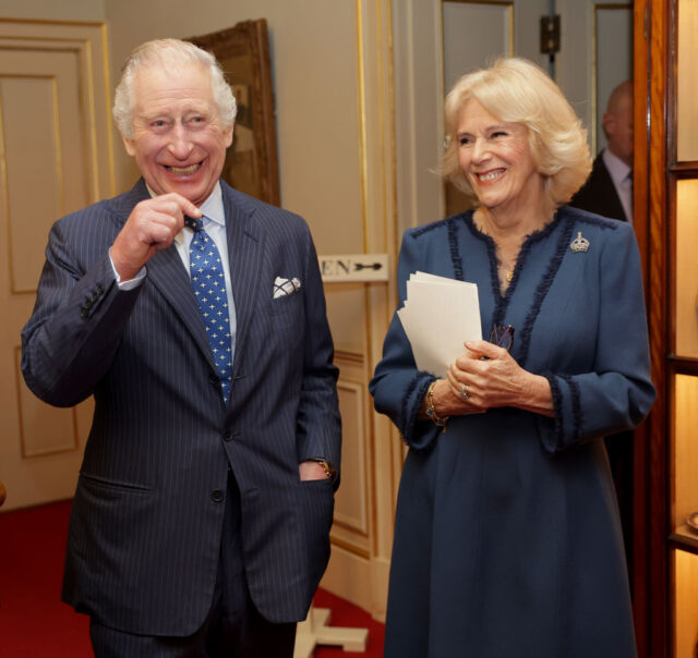 Charles and Camilla in formal wear laughing together in a hallway.