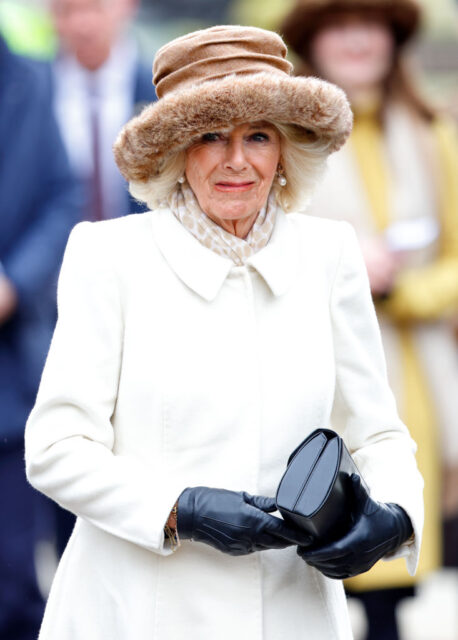 Camilla walking while wearing a white jacket, fur hat, and black gloves.
