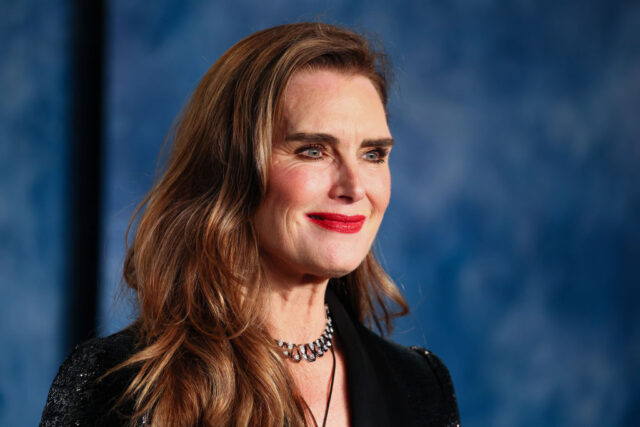 Brooke Shields smiling with a black top and bright red lipstick.