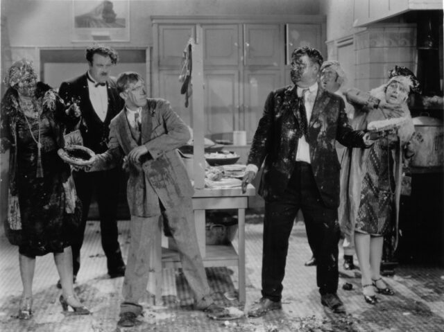 Photo showing Stan Laurel and Oliver Hardy preparing to throw pies at each other as other cast members look on. 