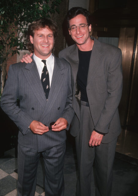 Dave Coulier and Bob Saget posing for a photo together wearing suits.