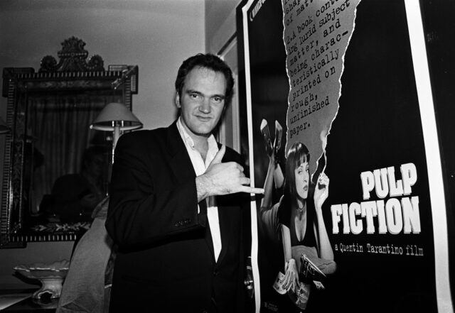 Quentin Tarantino standing in front of a 'Pulp Fiction' poster.