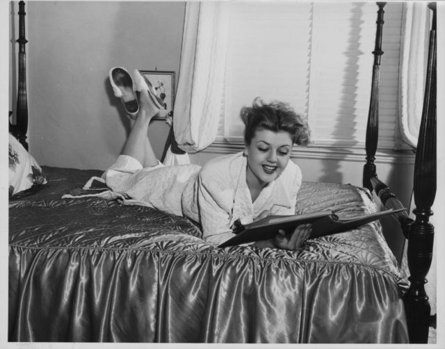 Portrait of actress Angela Lansbury, lying on a hotel bed wearing a bathrobe