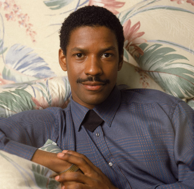 Portrait of Academy Award-winning American actor Denzel Washington seated on a sofa