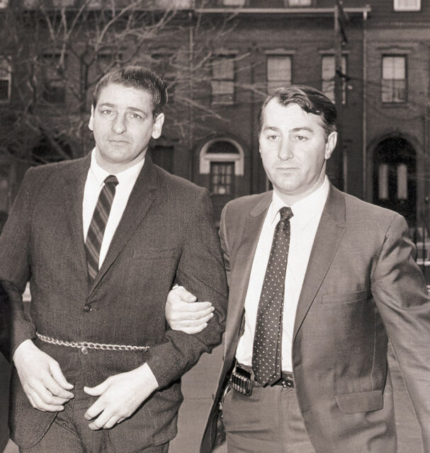 Albert DeSalvo in handcuffs being escorted by another man, both wear suits. 