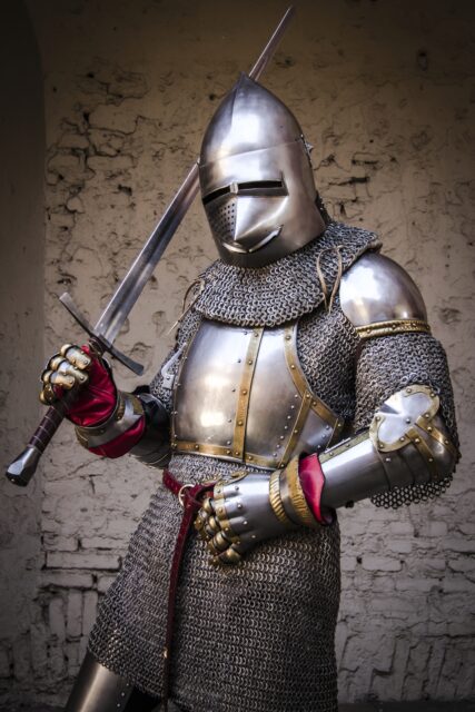A knight holding a sword up toward its shoulder, full helmet, chain mail, and armour.