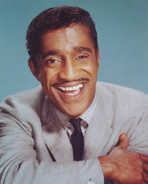 American actor, singer and dancer, Sammy Davis Jr. poses in front of a blue background