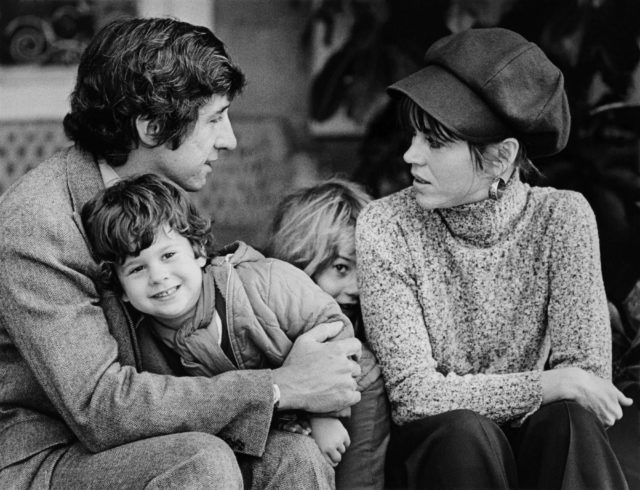 Jane Fonda with her husband Tom Hayden and their two children sit on the front porch in a black and white picture
