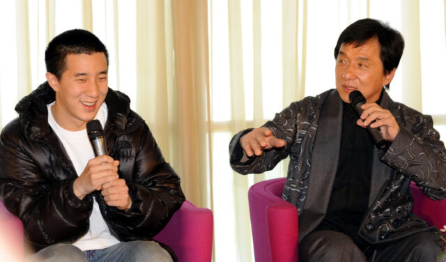 Jackie Chan and Jaycee Chan sitting in chairs and speaking into microphones.
