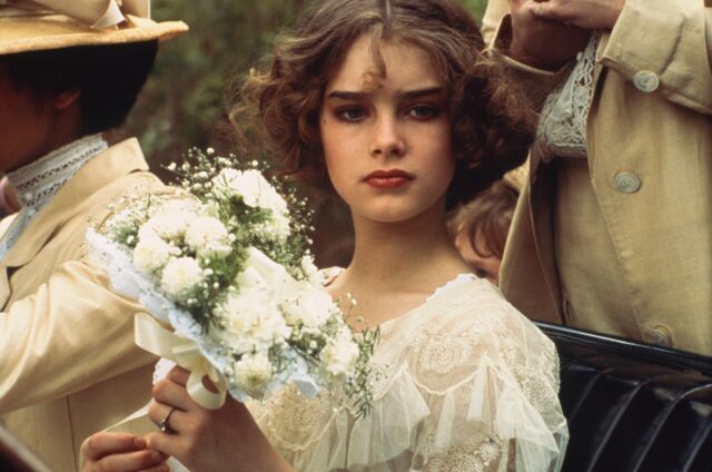Young Brooke Shields in a white dress holding a bouquet. 