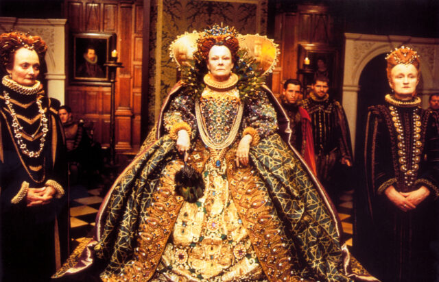 Judi Dench as Queen Elizabeth wearing an extravagant gown.