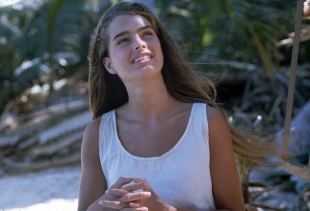 Young Brooke Shields on a tropical island in a white tank top.