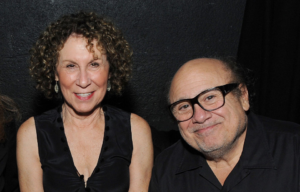 Rhea Perlman in a black shirt, and Danny Devito in a black shirt, pose together.