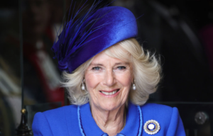 Camilla, Queen Consort smiling in a blue dress and hat.