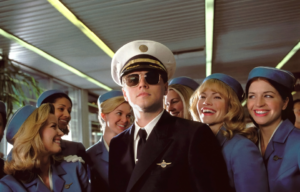 Leonardo DiCaprio dressed in a pilots uniform surrounded by flight attendants.