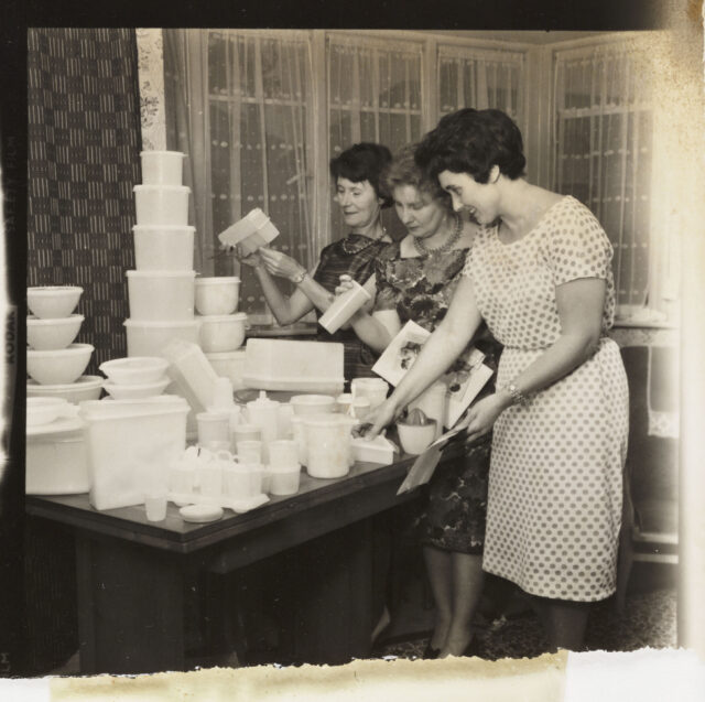 Three women standing at a table piled with Tupperware containers