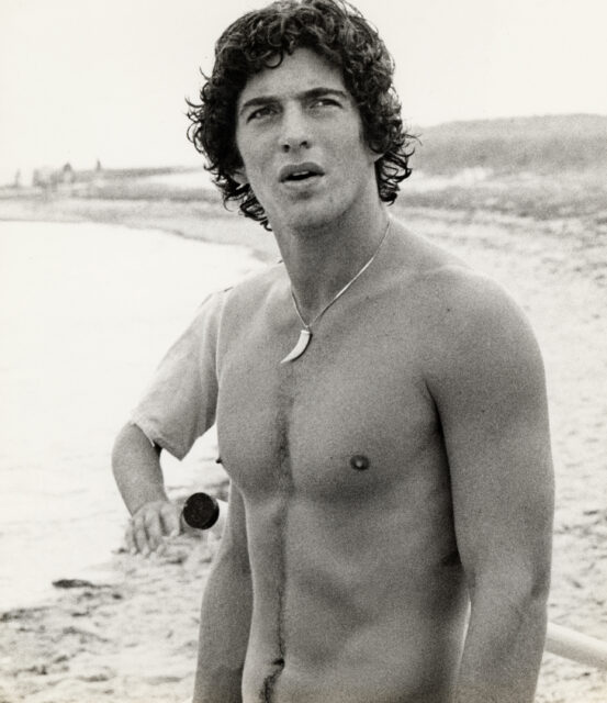 John F. Kennedy Jr. shirtless on a beach.