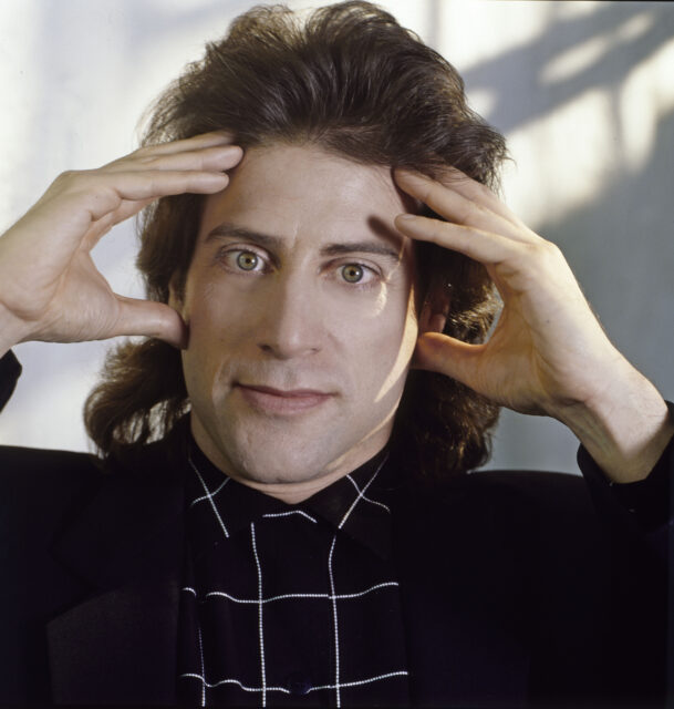 Headshot of Richard Lewis with his hands to his forehead.