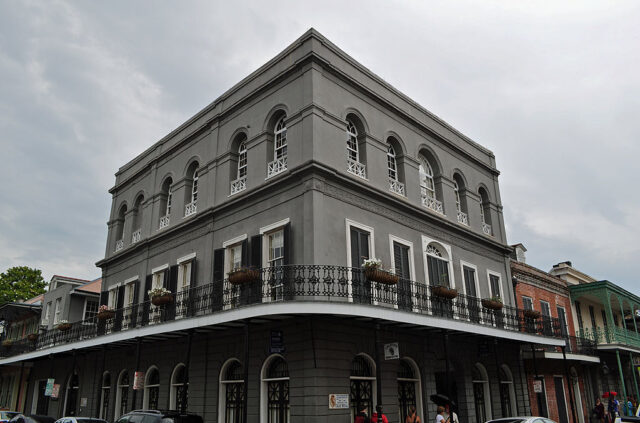 Three story grey building with a metal balcony on the second floor. 