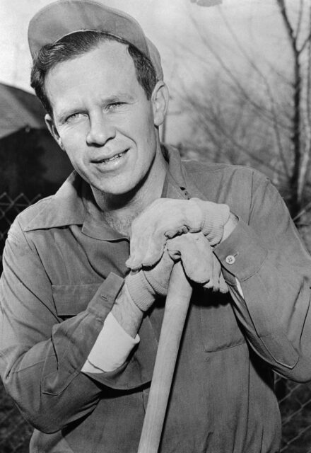 James Dougherty smiling for a photo while leaning on a shovel handle.