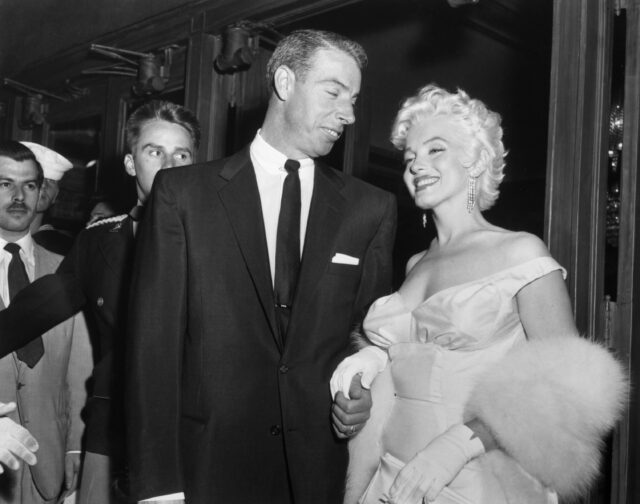 Marilyn Monroe looks on while holding hands with ex-husband Joe DiMaggio who looks at her while at the premiere of the film The Seven year Itch. 