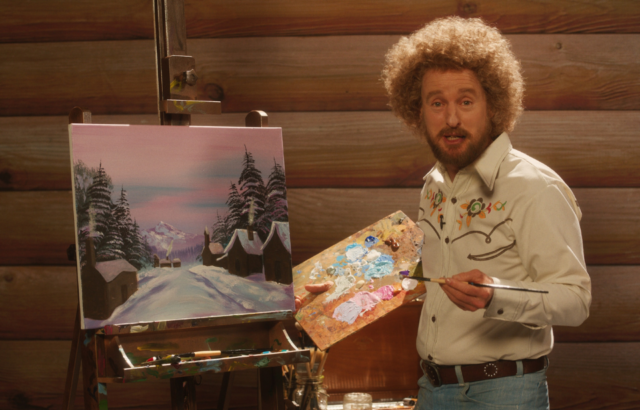 Owen Wilson standing in front of an easel holding a palette and paintbrush in the film 'Paint'