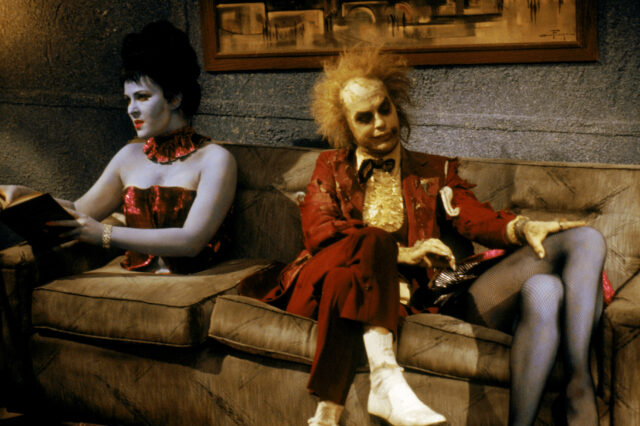 Michael Keaton as Beetlejuice sitting beside a woman sliced in half.