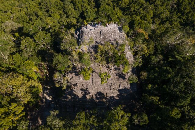 Aerial view of a Mayan pyramid structure surrounded by jungle.