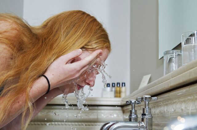 A woman washing her face in a sink.