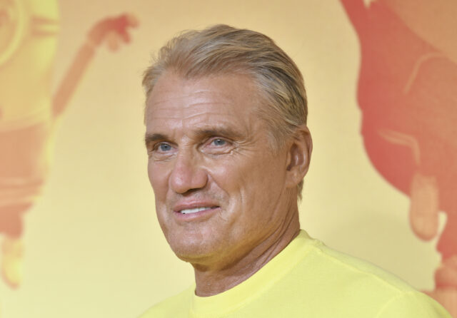 Headshot of Dolph Lungren wearing a yellow shirt against a yellow background.