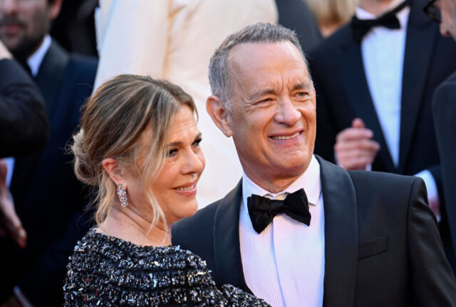 Rita Wilson, in a sparkling black dress, and Tom Hanks, in a black suit, pose for a photo together.