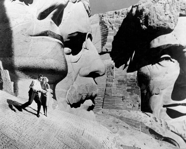 Cary Grant and Eva Marie Saint hold each other while standing on a fake set of Mount Rushmore.