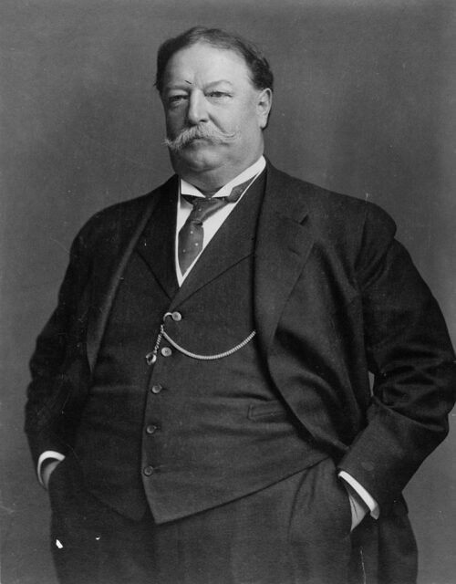 William Howard Taft in a black suit and waistcoat with his hands in his pockets.